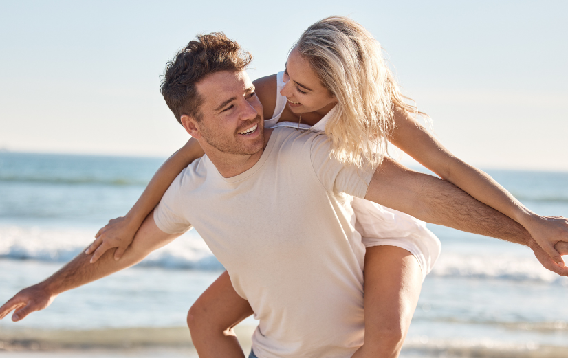 Verliefde man en vrouw samen op het strand, naar elkaar lachend en denkend aan hun favoriete supplementen voor op vakantie.