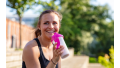 Vrouw in sportkleding heeft berekend hoeveel gram eiwitten ze per dag nodig heeft en drinkt een eiwitshake na haar training.