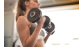 Vrouw lift dumbbells en traint populaire fitnessoefeningen in de sportschool.