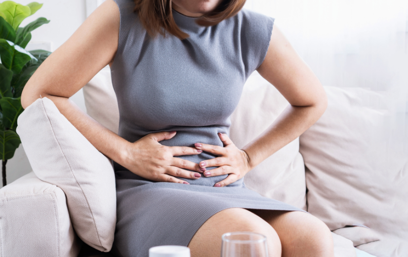 Vrouw met Prikkelbare Darm Syndroom zit op de bank en grijpt naar haar pijnlijke buik, zich afvragend wat ze eraan kan doen.