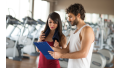 Personal trainer laat sportschema zien aan vrouw met oefeningen om te helpen haar sportroutine op te bouwen.