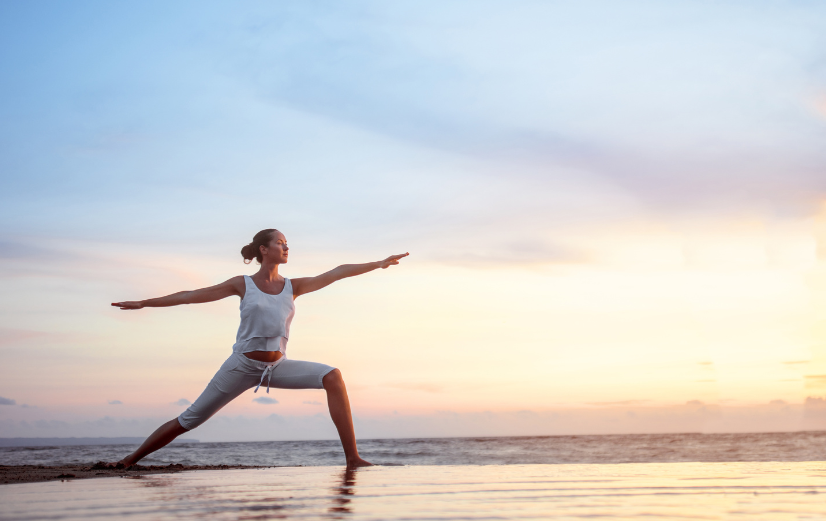 Vrouw doet yoga op het strand tijdens zonsopkomst om te blijven sporten op vakantie.