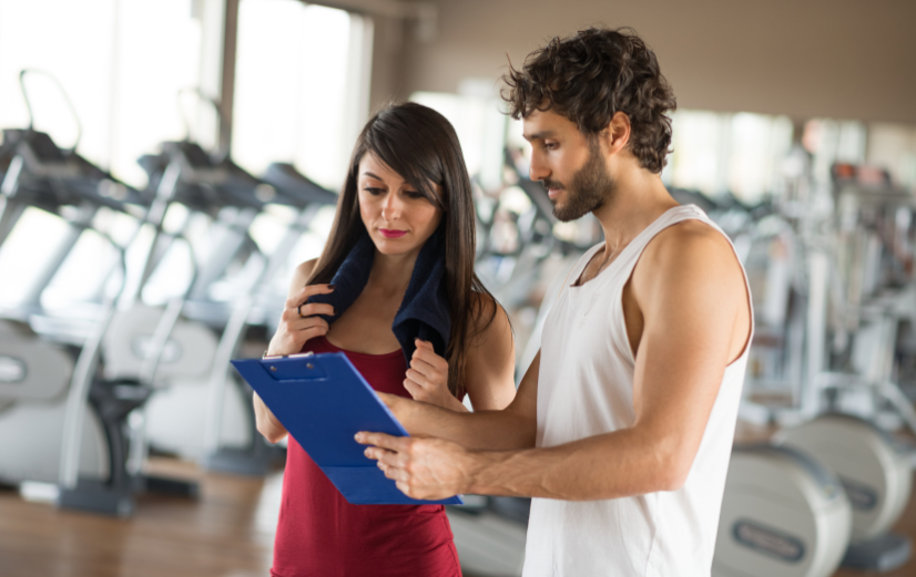 Personal trainer laat sportschema zien aan vrouw met oefeningen om te helpen haar sportroutine op te bouwen.
