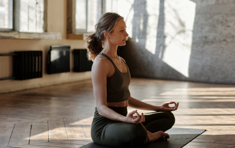 Vrouw met sportkleding aan zit in een yogahouding op de vloer en vraagt zich af waar magnesium goed voor is.